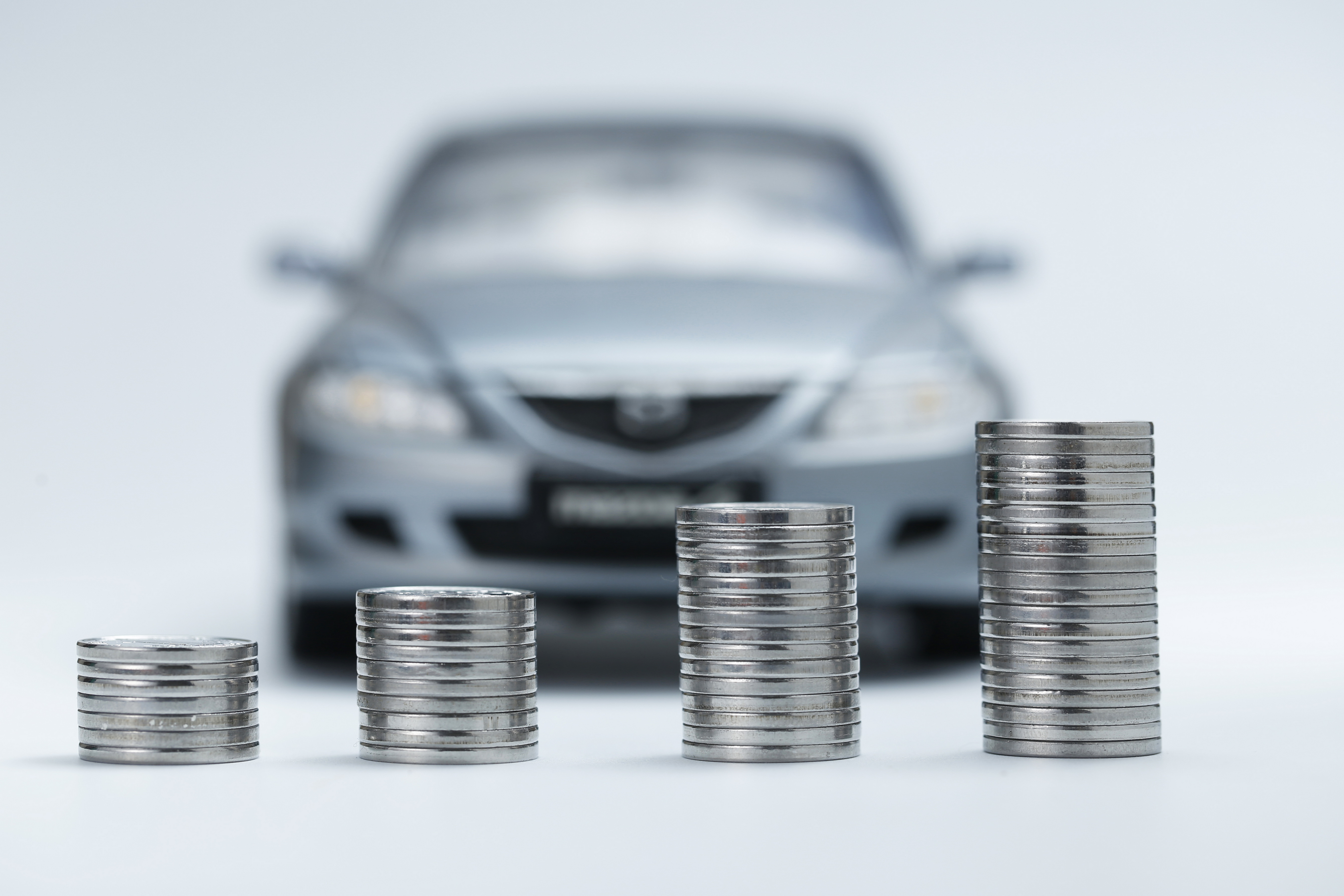 Coins stacked in front of a car. Car loans provided by IndoStar Capital Finance